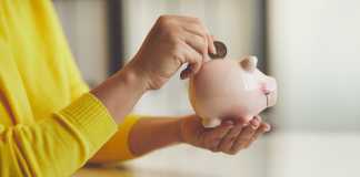 Close up of woman puts euro coin into piggy bank