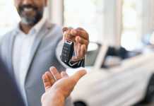 Closeup hand of cardealer giving new car key to customer. Detail of salesman hand giving keys to a client at showroom. Man's hand receiving car keys from african agent in a auto dealership with copy space.