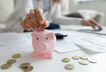 Close up coffee table lot of invoice, financial stats documents, utility bills, household payments, focus on female hand puts coin in piggy bank. Family budget manage, making personal savings concept