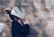 School Girl with Book in front of natural rustic red brick background holding book up to her face