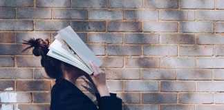 School Girl with Book in front of natural rustic red brick background holding book up to her face