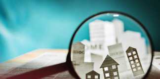 A Brief Glossary of Real Estate Terms Magnifying glass in front of an open newspaper with paper houses. Concept of rent, search, purchase real estate.