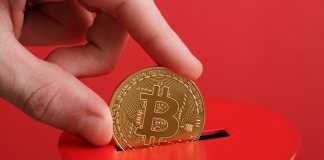 Bitcoin of Whale Definition Kiev, Ukraine - May 16, 2021: Men hand puts gold coin with bitcoin symbol into slot of red donation box. Concept crypto currency. Selective focus