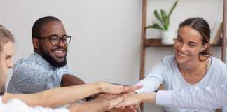 Happy smiling corporate diverse team joining hands together showing unity