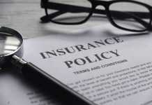 Selective focus of magnifying glass,glasses and Insurance Policy letter on a white wooden background.