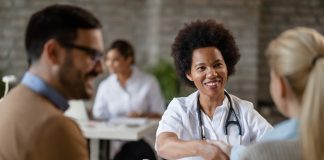 Happy African American doctor shaking hands with a couple after medical appointment at clinic.