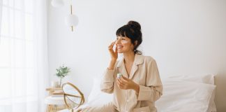 Smiling woman applying face cream sitting on bed