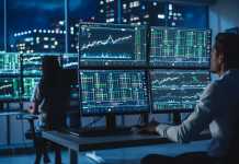 Financial Analyst Working on a Computer with Multi-Monitor Workstation with Real-Time Stocks, Commodities and Foreign Exchange Charts. Businessman Works in Investment Bank City Office at Night.