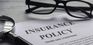 Selective focus of magnifying glass,glasses and Insurance Policy letter on a white wooden background.