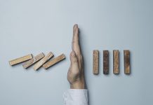 Businessman hand protecting rectangle block which falling to stop dominos others rectangle standing on blue background. Risk and crisis management concept.
