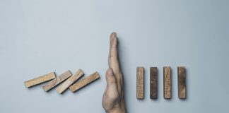 Businessman hand protecting rectangle block which falling to stop dominos others rectangle standing on blue background. Risk and crisis management concept.