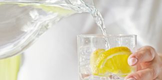 Female hands pouring water from the decanter into a glass beaker with lemon and ice. Health and diet concept. Quenching thirst on a hot day.
