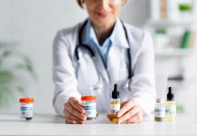 cropped view of doctor in white coat holding bottles with cbd and medical cannabis lettering
