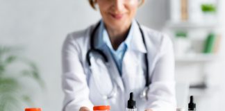 cropped view of doctor in white coat holding bottles with cbd and medical cannabis lettering