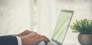 Closeup businessman hands working use laptop finance business document reading report paperwork spreadsheet at office desk. Man hands type keyboard write on office note check financial graph chart