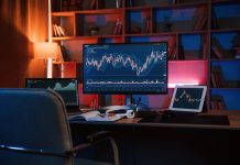 Computer with stock exchange graph on display is in the dark room with neon lighting
