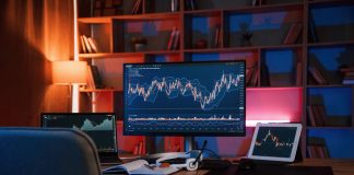 Computer with stock exchange graph on display is in the dark room with neon lighting