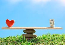 Red heart and dollar bills on the scales of stones and board on a blue sky background