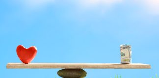 Red heart and dollar bills on the scales of stones and board on a blue sky background