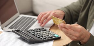 Man holding credit card while using calculator