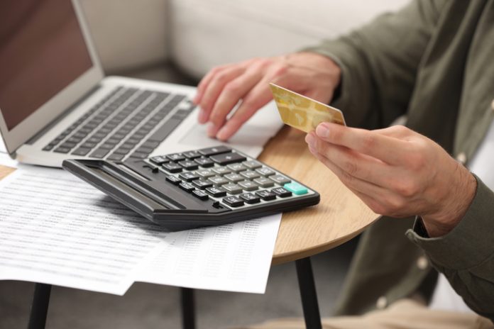 Man holding credit card while using calculator