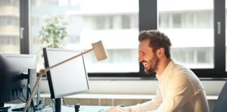 Businessman Sitting on Black Rolling Chair While Facing Black Computer Set and Smiling