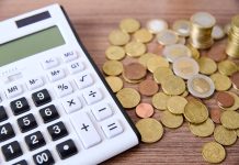 A wooden table with a glass jar containing coins and a calculator situated on top