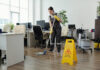 Female cleaner in workwear using mop while cleaning floor in office