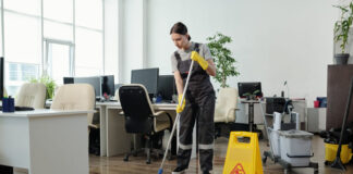 Female cleaner in workwear using mop while cleaning floor in office