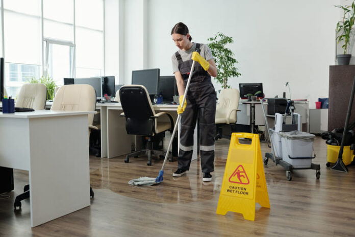 Female cleaner in workwear using mop while cleaning floor in office