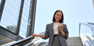 Smiling young Asian business woman standing on escalator using phone
