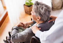 Health visitor and a senior woman during home visit. Unrecognizable nurse giving woman shoulder massage.