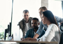 Friendly creative diverse colleagues team discuss online project use computer at workplace