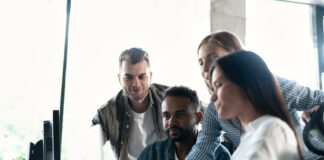 Friendly creative diverse colleagues team discuss online project use computer at workplace