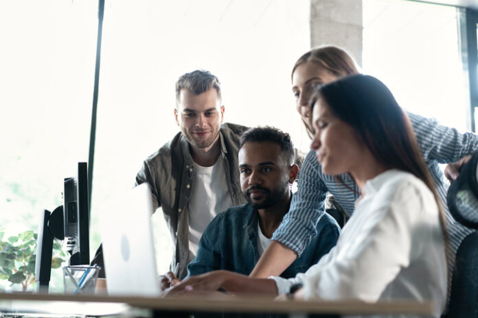 Friendly creative diverse colleagues team discuss online project use computer at workplace