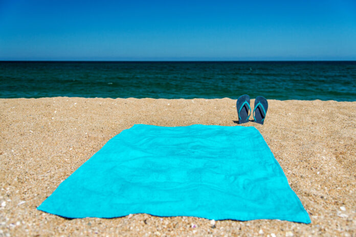 Blue sandal flip flop and towel on yellow sand