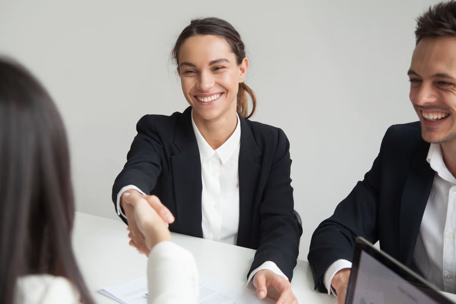 Smiling female hr handshaking businesswoman at group meeting or interview 