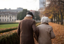 A rear view of senior couple on walk outdoors in park in autumn.