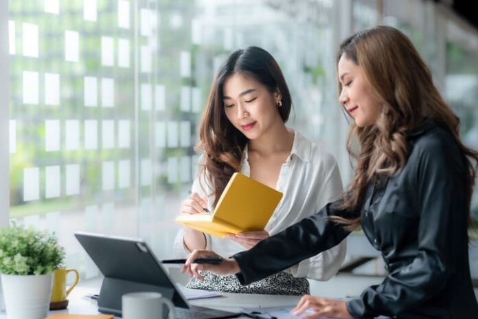 Two Asian businesswoman working pointing laptop computer and discussing documents and idea at meeting