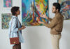 Young man discussing modern art with young woman during exhibition in gallery