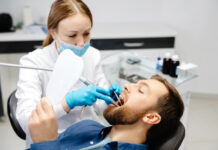 A handsome man is sitting in a chair at a woman's appointment at the dentist's office.