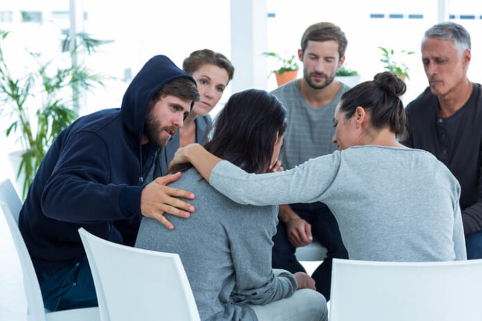 Concerned patients comforting another in rehab group at a therapy session