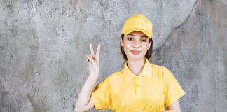 Female service agent in yellow uniform standing on concrete wall and sending peace.