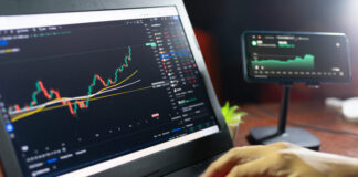Trader at home office trading on computer and using mobile phone.