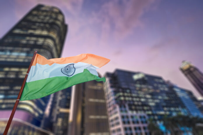 A large green, white and red Indian flag is flying in the air above a city.