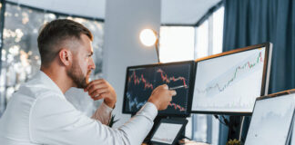 Young businessman in formal clothes is with multiple screens for trading