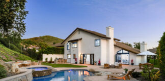 Modern luxury house with a swimming pool and patio area, surrounded by greenery and a clear evening sky.