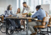Selective focus of smiling disabled businessman and colleagues in office.