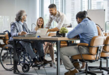 Selective focus of smiling disabled businessman and colleagues in office.