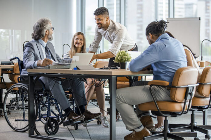 Selective focus of smiling disabled businessman and colleagues in office.
